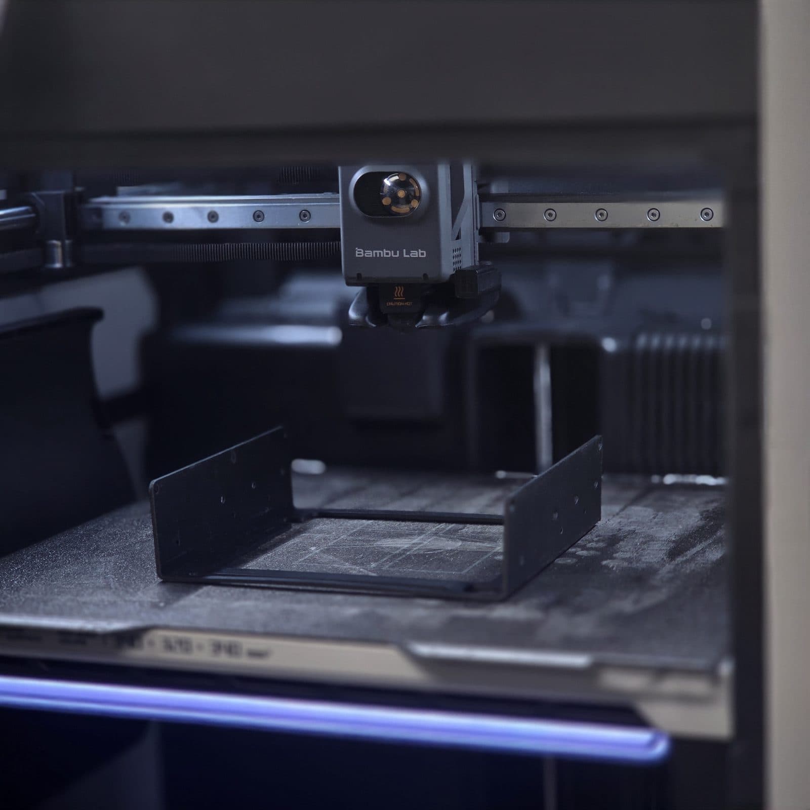 A black FDM printed part being printed on the Bambu Lab H2S build plate