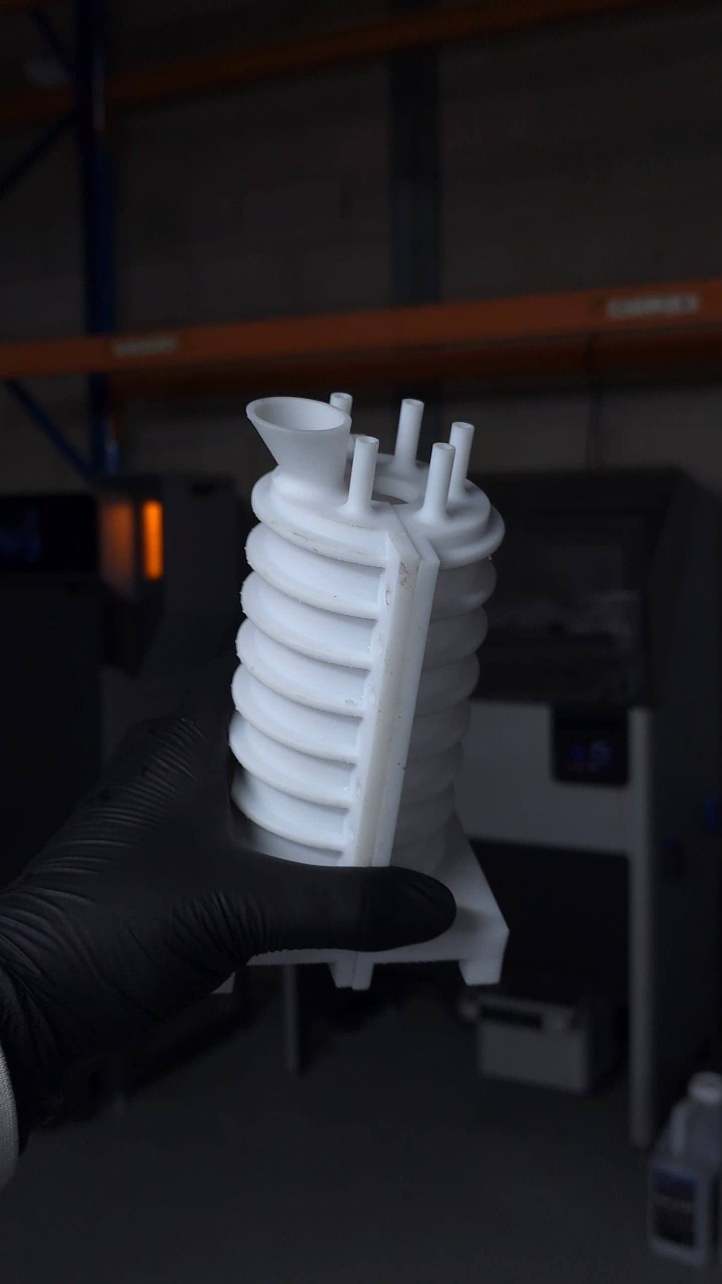 A white 3D printed two-part mould shell with a pour funnel and vent pipes, held in a gloved hand in the Insera 3D workshop