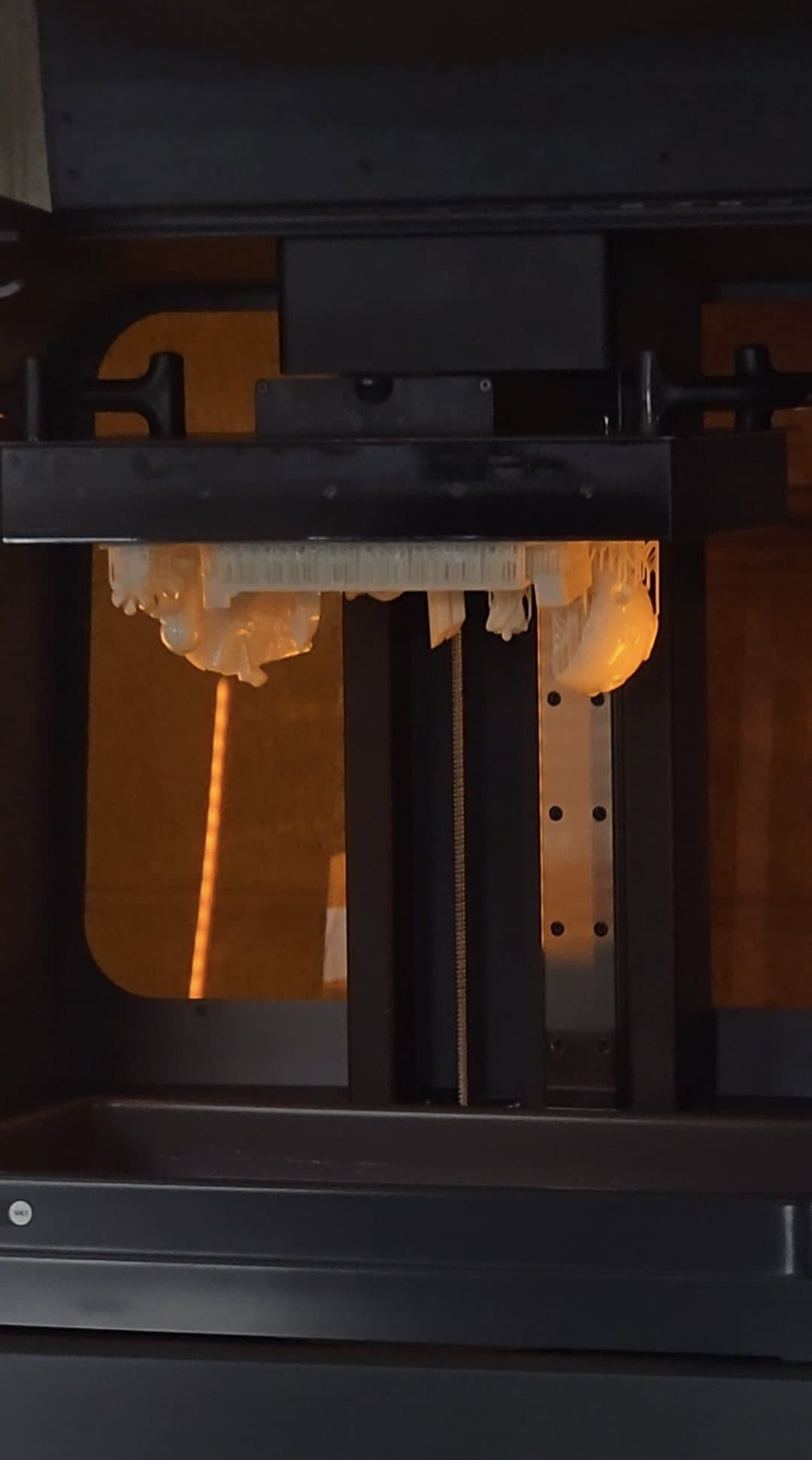 A finished build of white resin parts on their supports, hanging from the build platform inside a Formlabs Form 3L