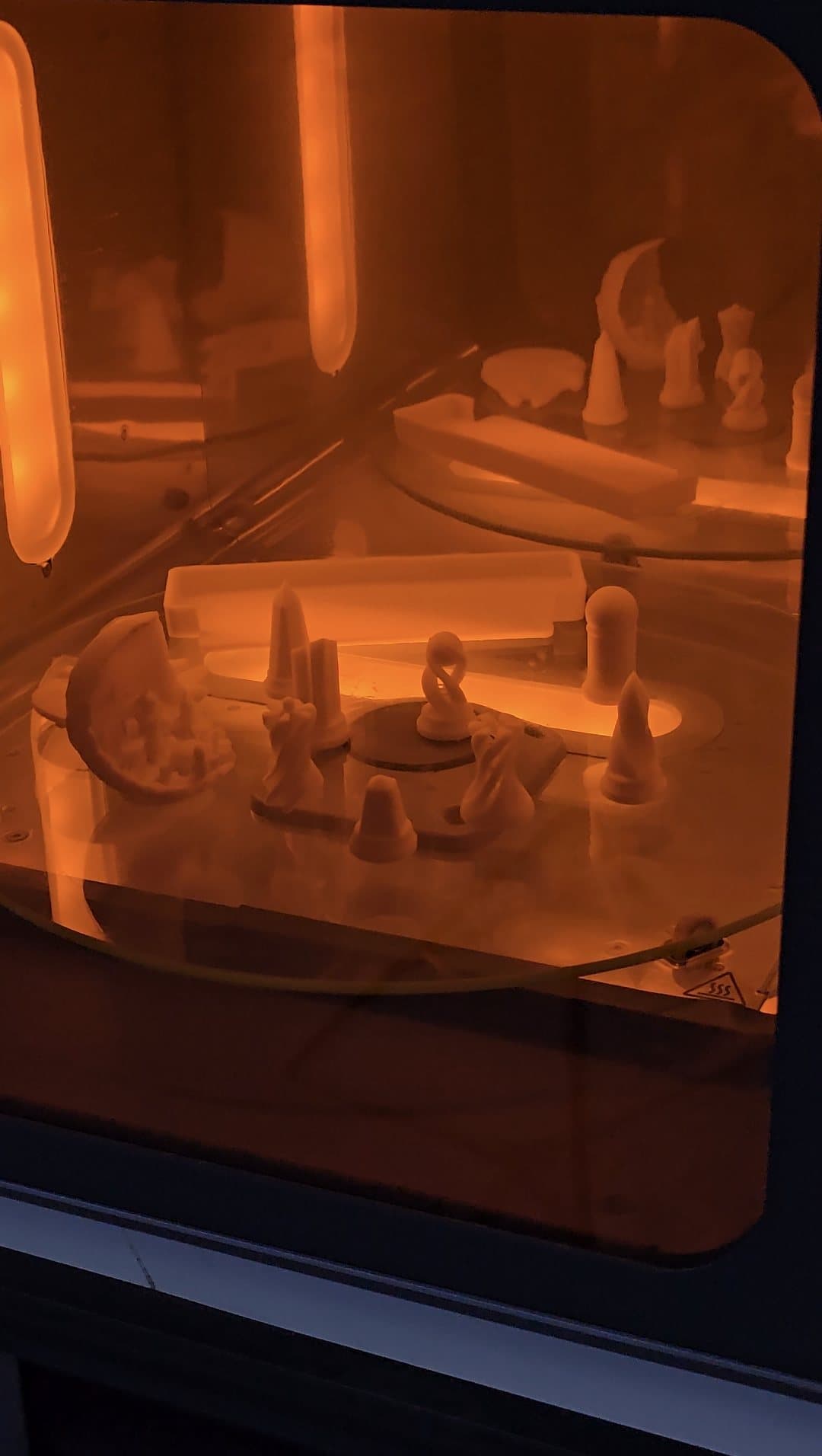 White resin 3D printed parts curing under orange-filtered UV light on the turntable of a Formlabs Form Cure