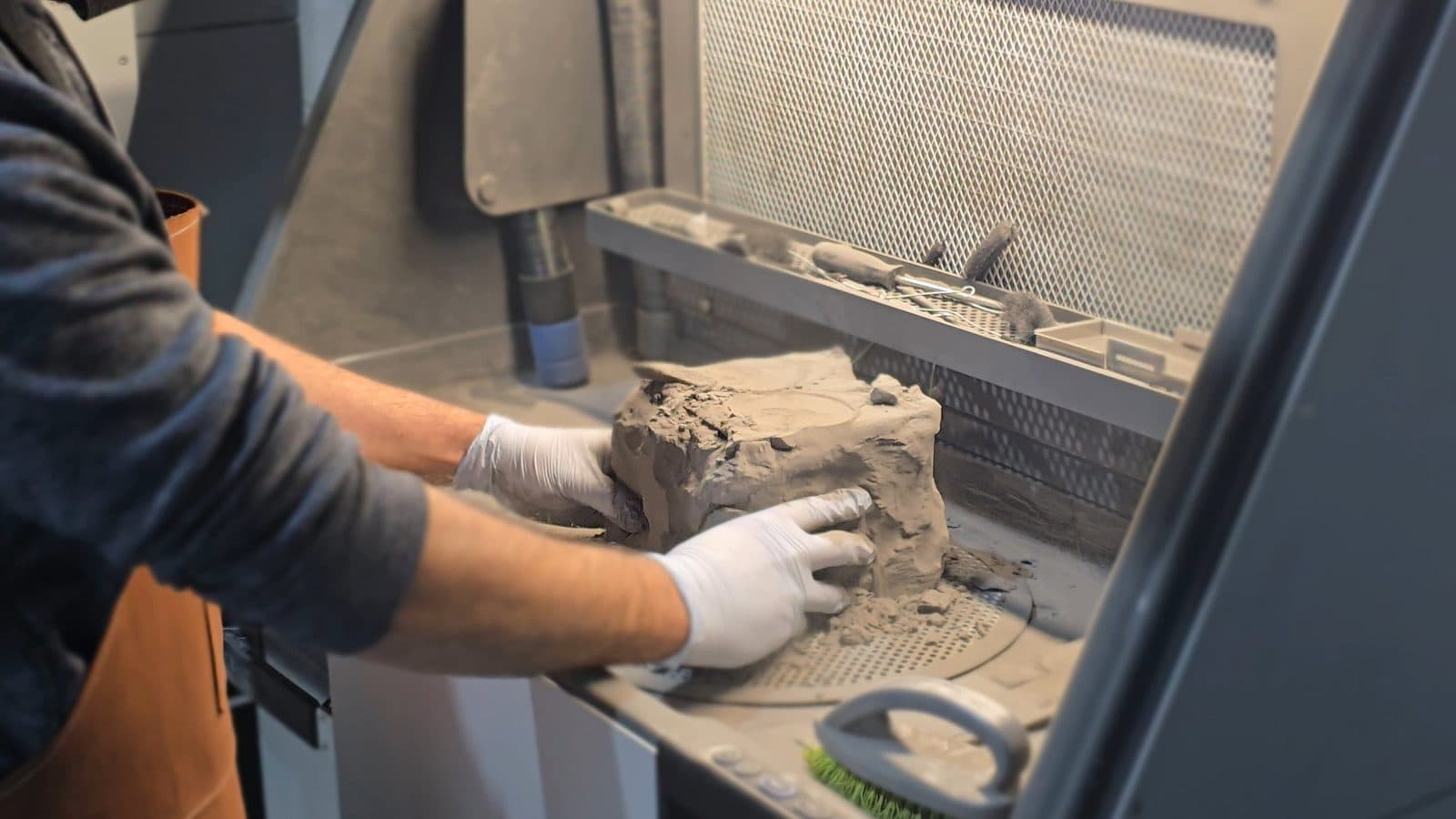 Gloved hands breaking printed parts out of the powder cake at the Fuse Sift